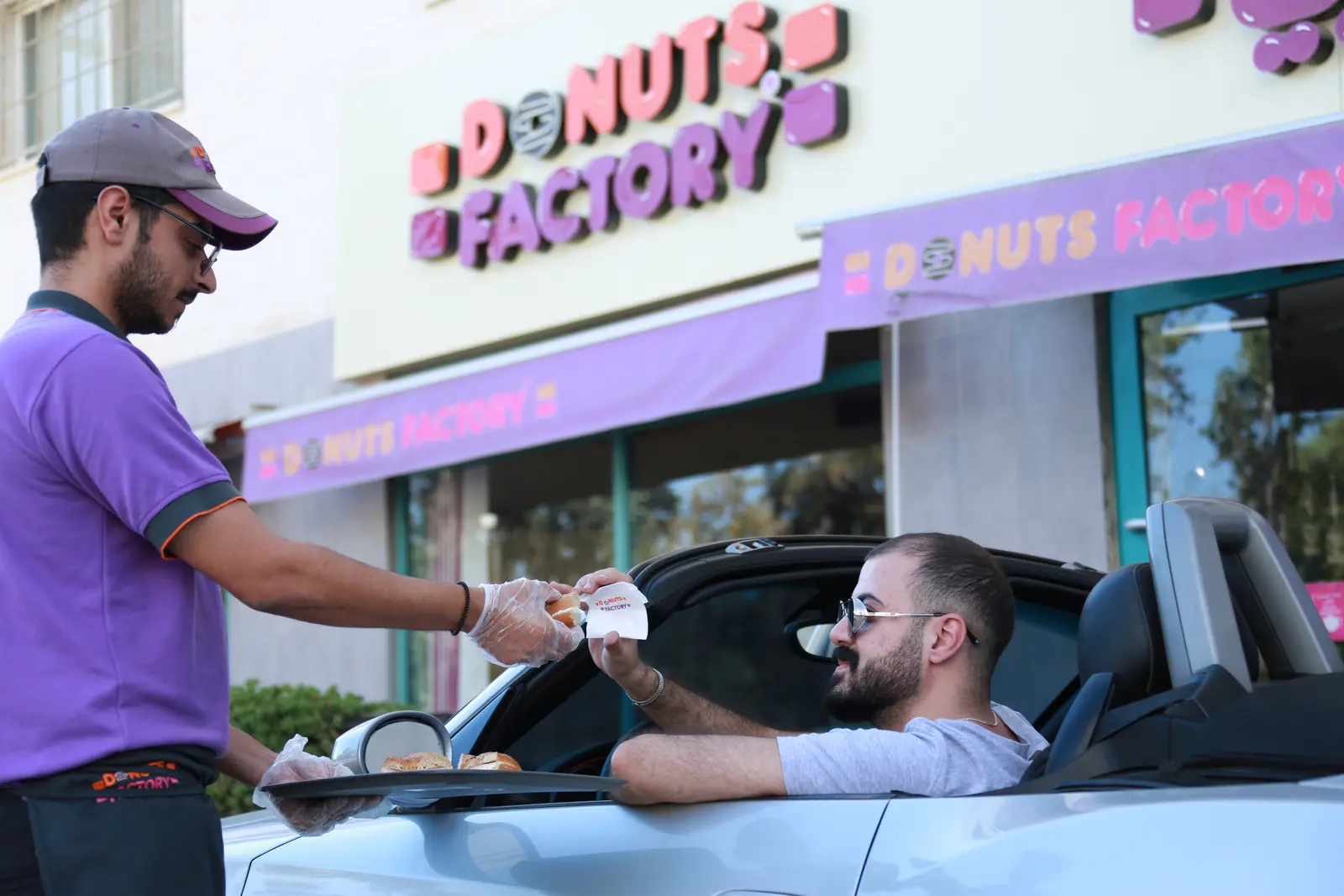 A Donuts Factory team member serving a customer outside a store